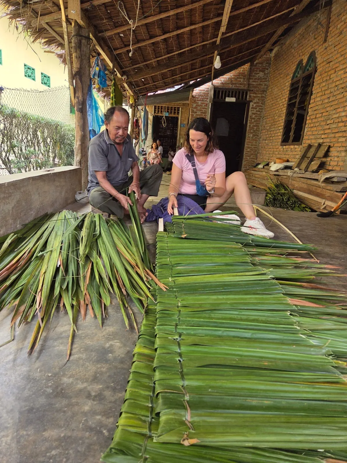 Marion s'initie au tressage du toit en feuilles de palmier (atap) avec un villageois de Bukit Lawang